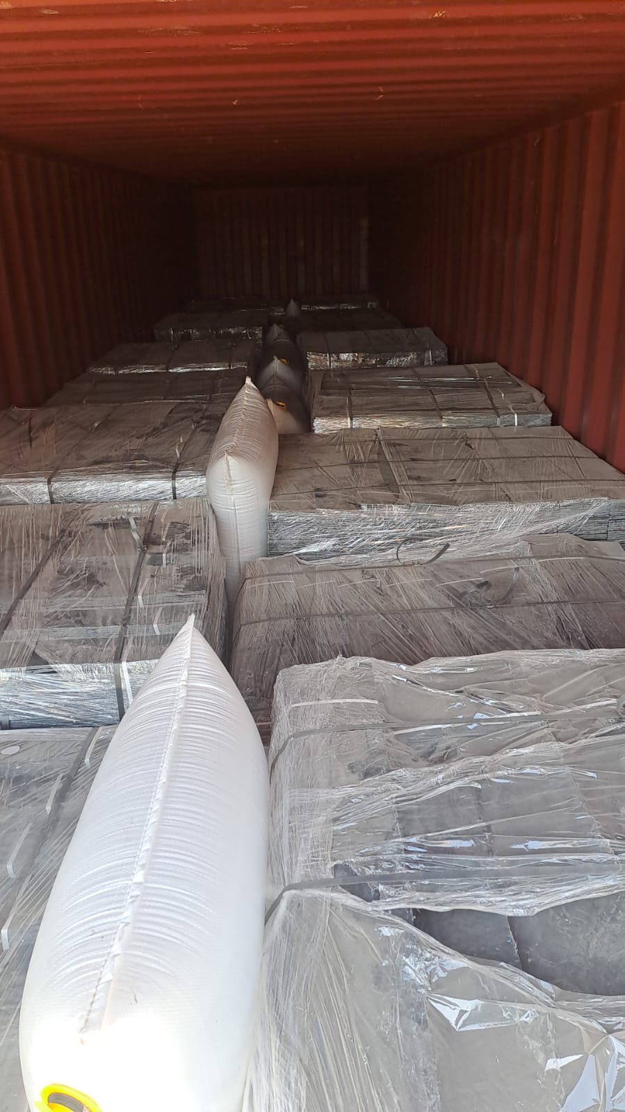 Shrink-wrapped pallets of cover plates loaded in a 40-foot container with dunnage air bags